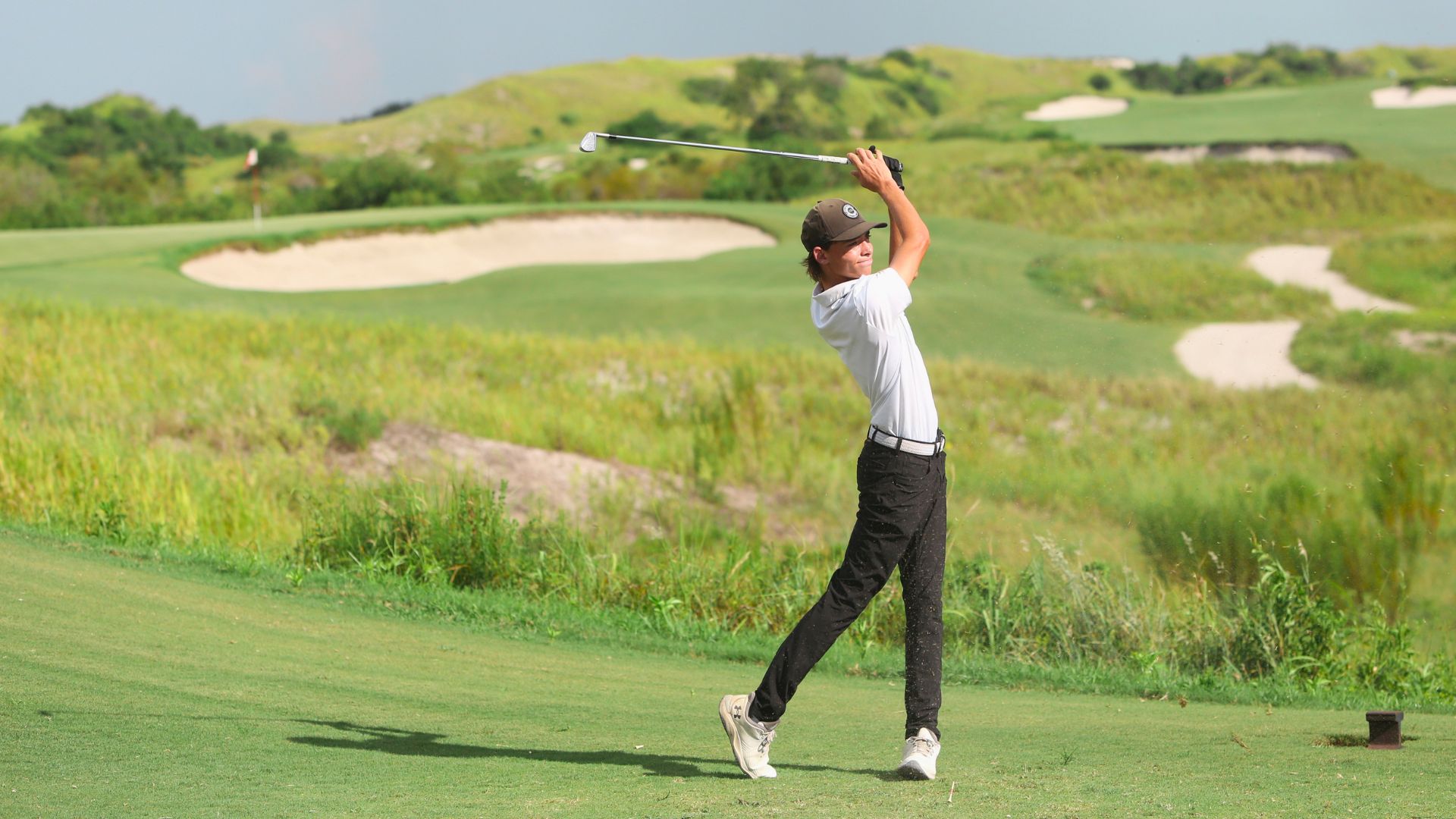 Junior golfer mid-swing on a coastal links course